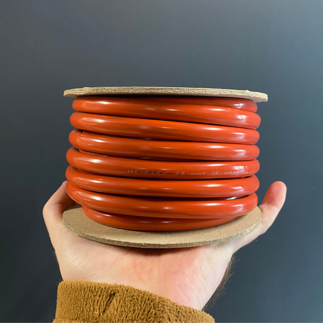 A hand holding a spool of bright orange-red welding cable electrical wire against a dark gray background.