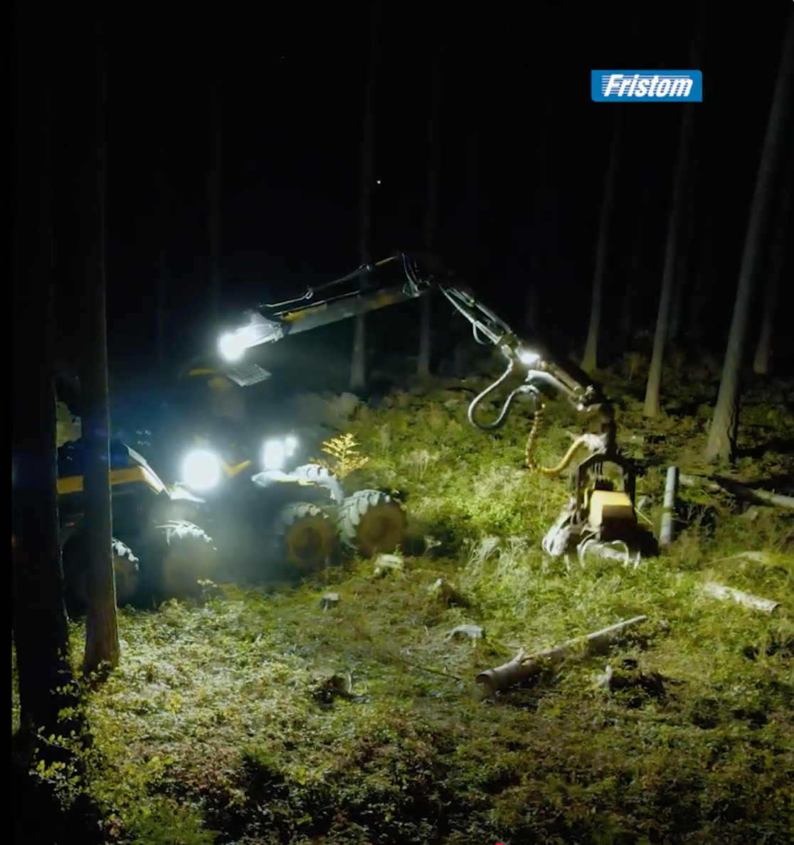 Excavator operating in a forest at night with 'Fristom' branding.