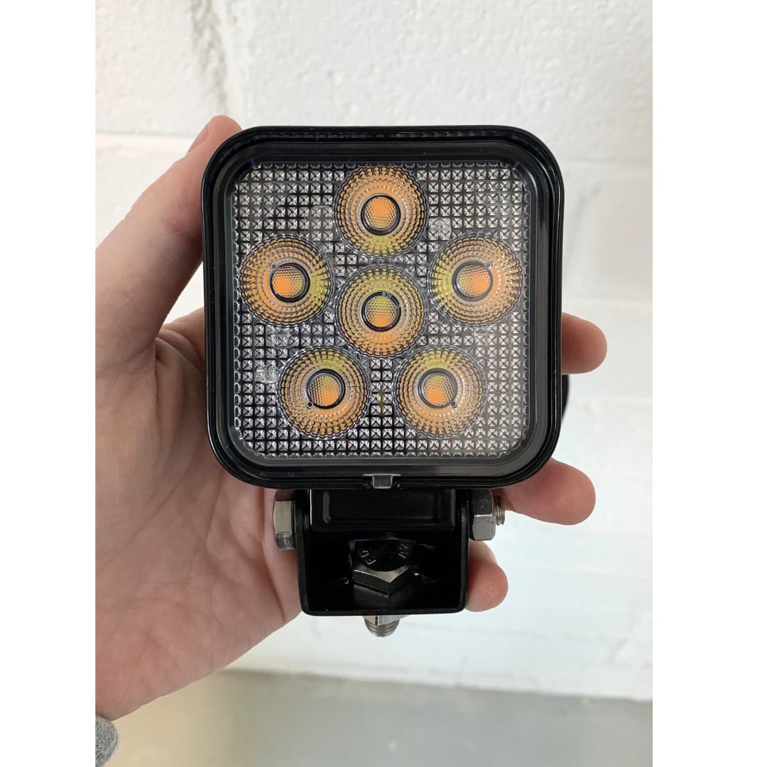 Hand holding a square LED work light with multiple yellow lights on a white background UK + Ireland